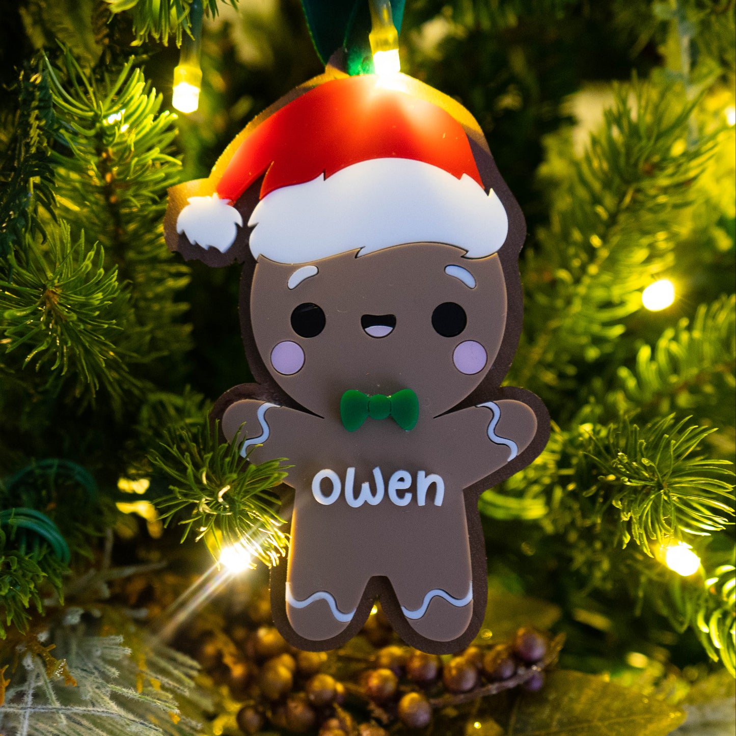 Personalized gingerbread boy ornament hanging on a Christmas tree, acrylic design with red bow and custom name, holiday kids keepsake with Bible verse on back