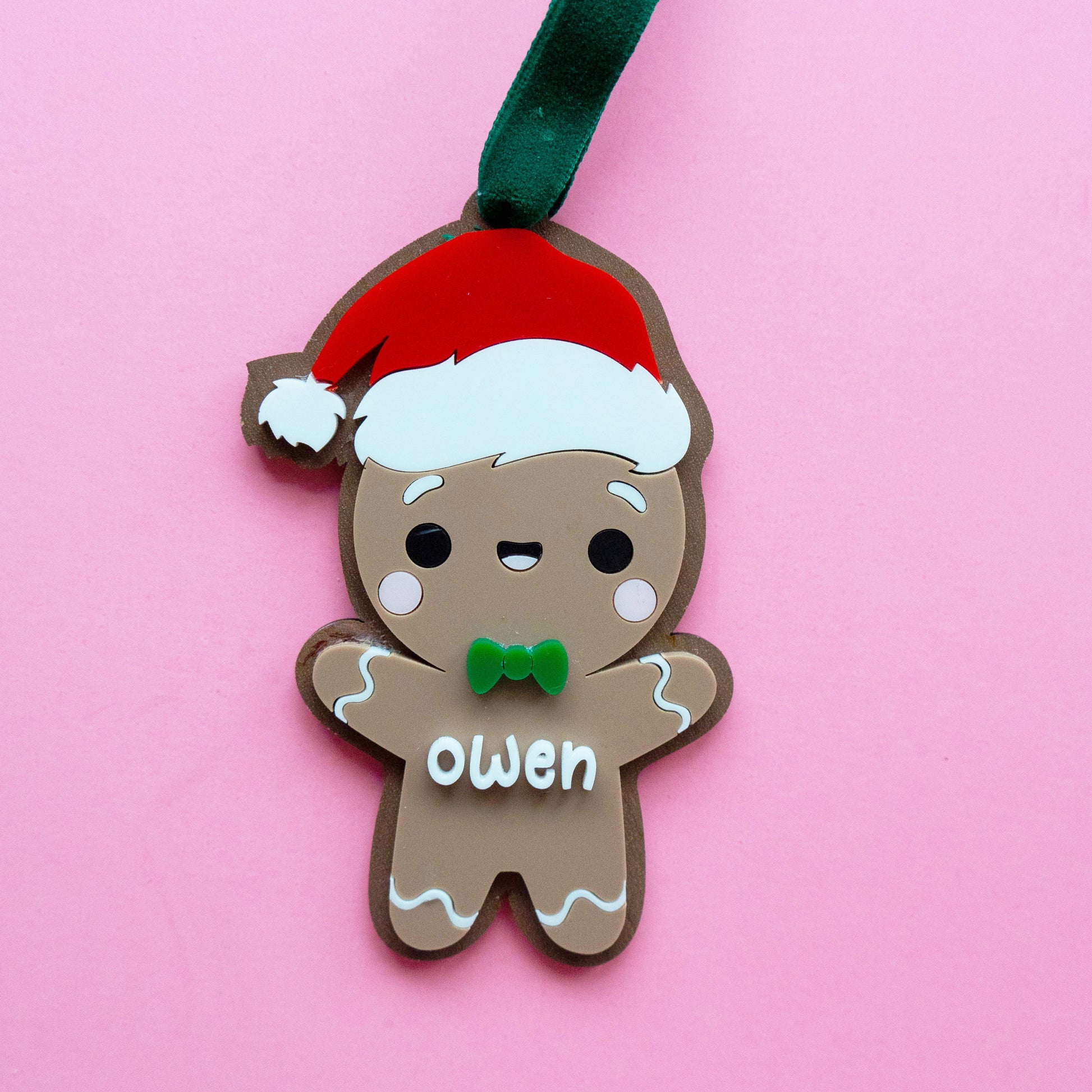 Gingerbread boy Christmas ornament made of layered acrylic with a Santa hat and custom name “Owen,” personalized ornament with Bible verse on the back.