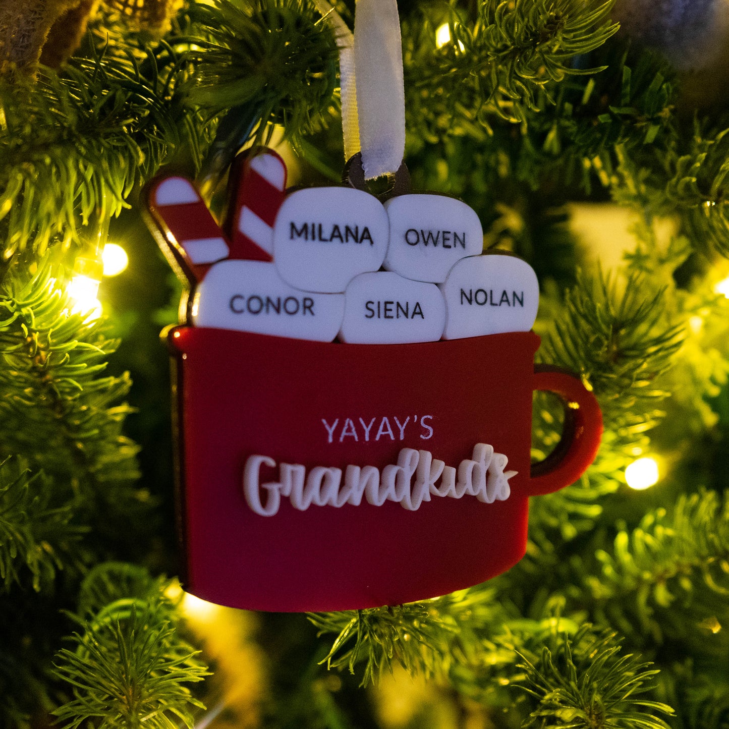 Personalized hot cocoa ornament on a Christmas tree with marshmallows showing grandkids’ names and a Bible verse engraved on the back, Christian grandparent keepsake.