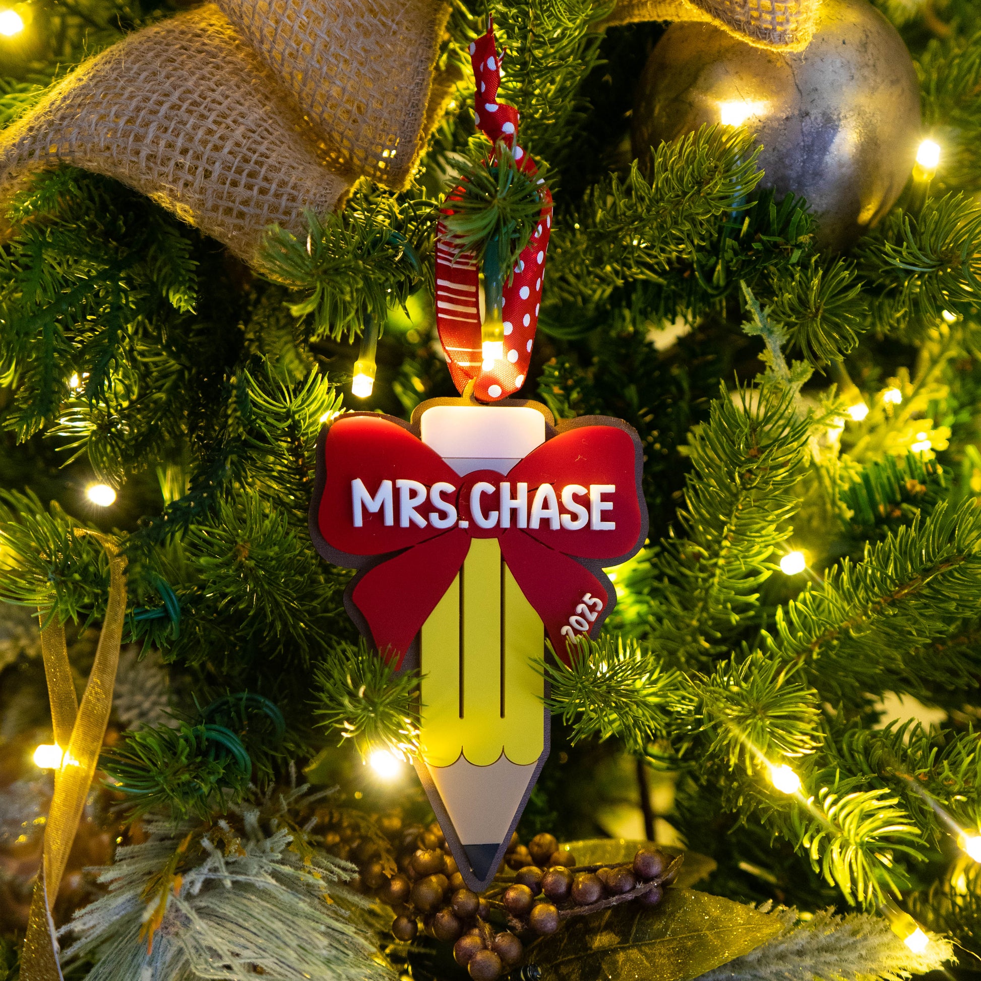 Personalized teacher pencil ornament with red bow, teacher name “Mrs. Chase,” red polka-dot ribbon, hanging in Christmas tree.