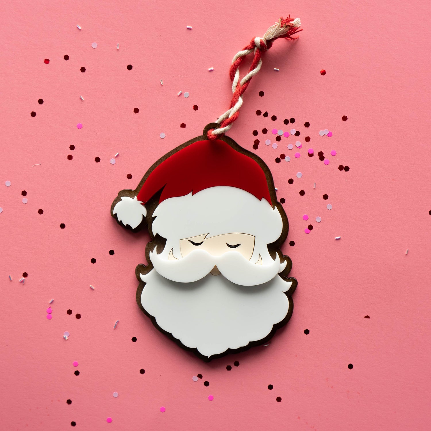 Front of layered acrylic Santa ornament with festive string on pink background — Curio & Co.