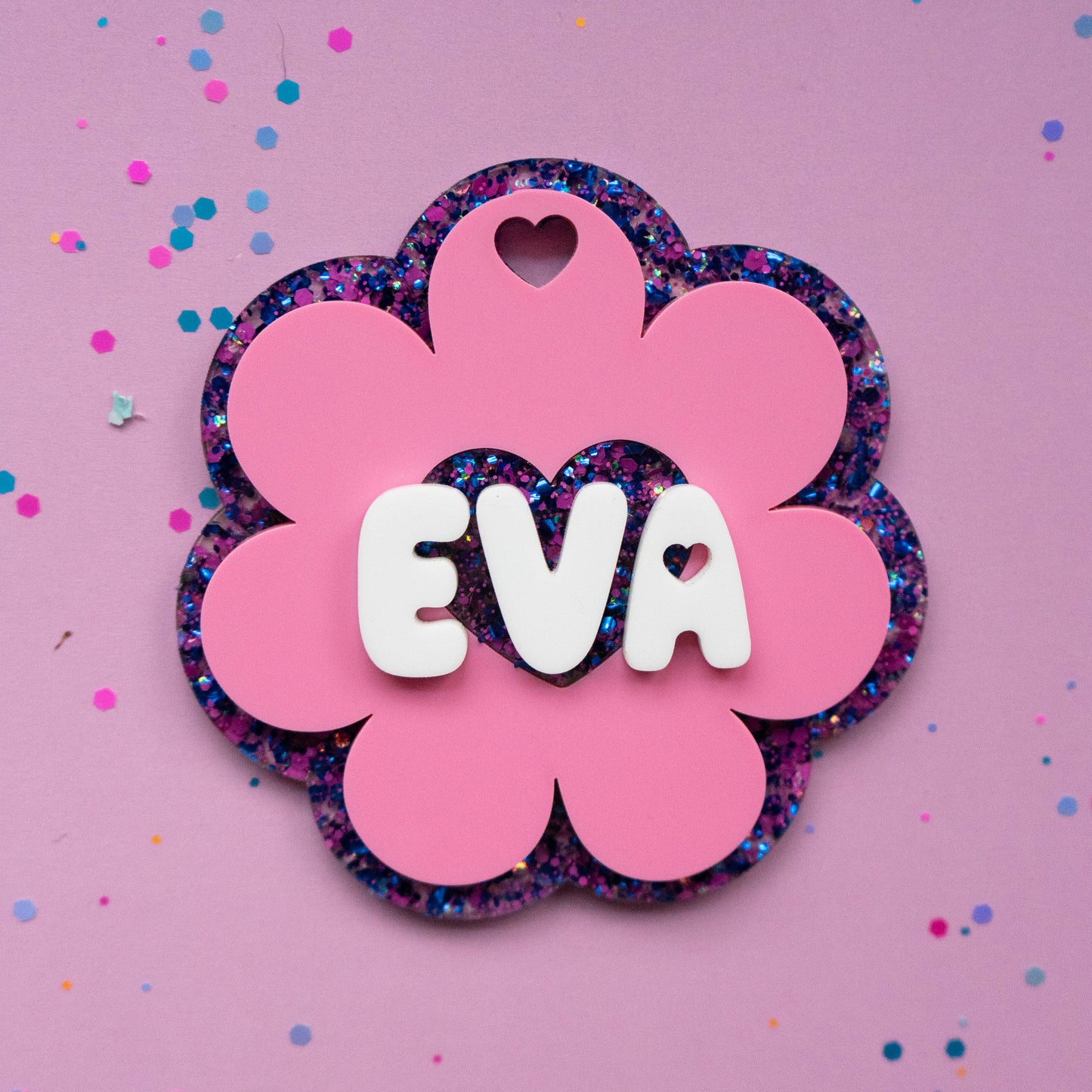Pink flower glitter name tag with white 3D letters spelling EVA on purple background with confetti — Curio & Co.