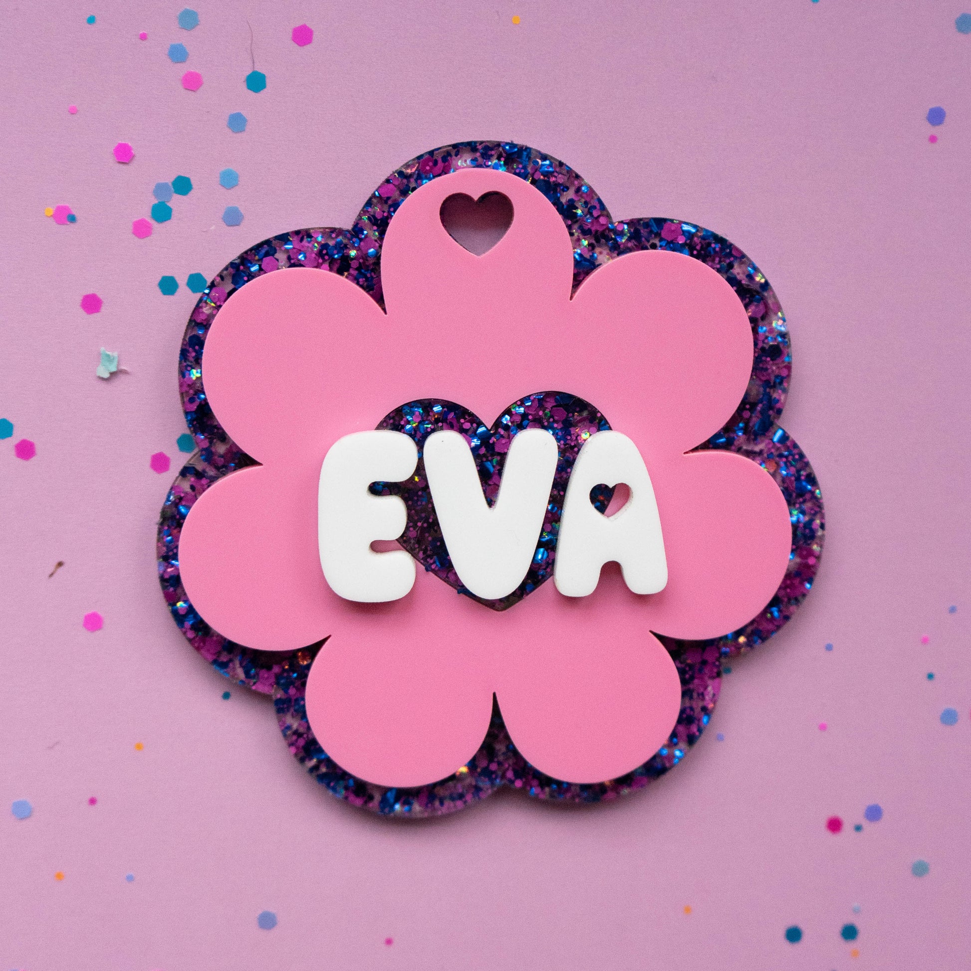 Pink flower glitter name tag with white 3D letters spelling EVA on purple background with confetti — Curio & Co.