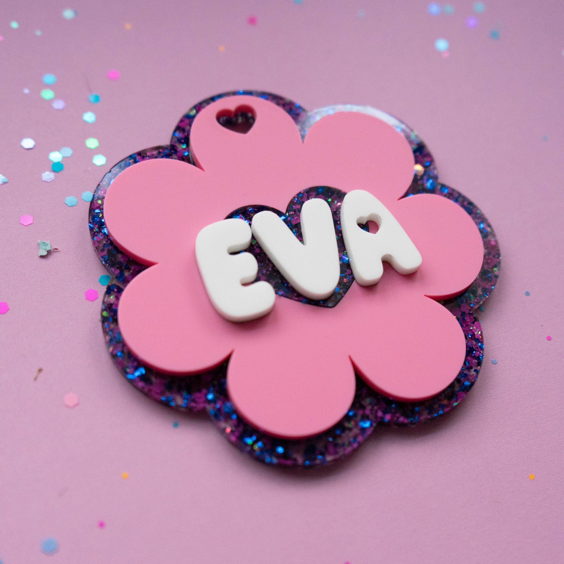 Pink flower glitter name tag with white 3D letters spelling EVA on purple background with confetti — Curio & Co.