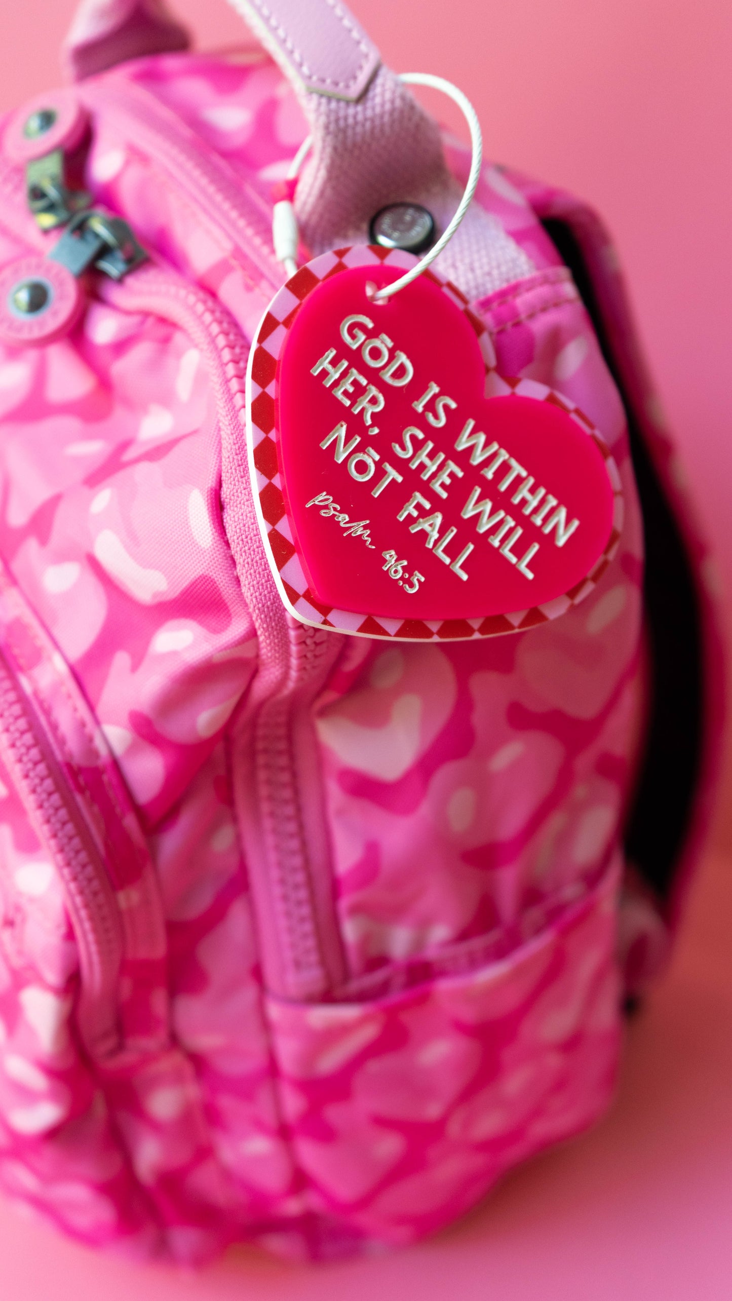 Pink backpack with a heart-shaped tag featuring a bible verse on a pink background
