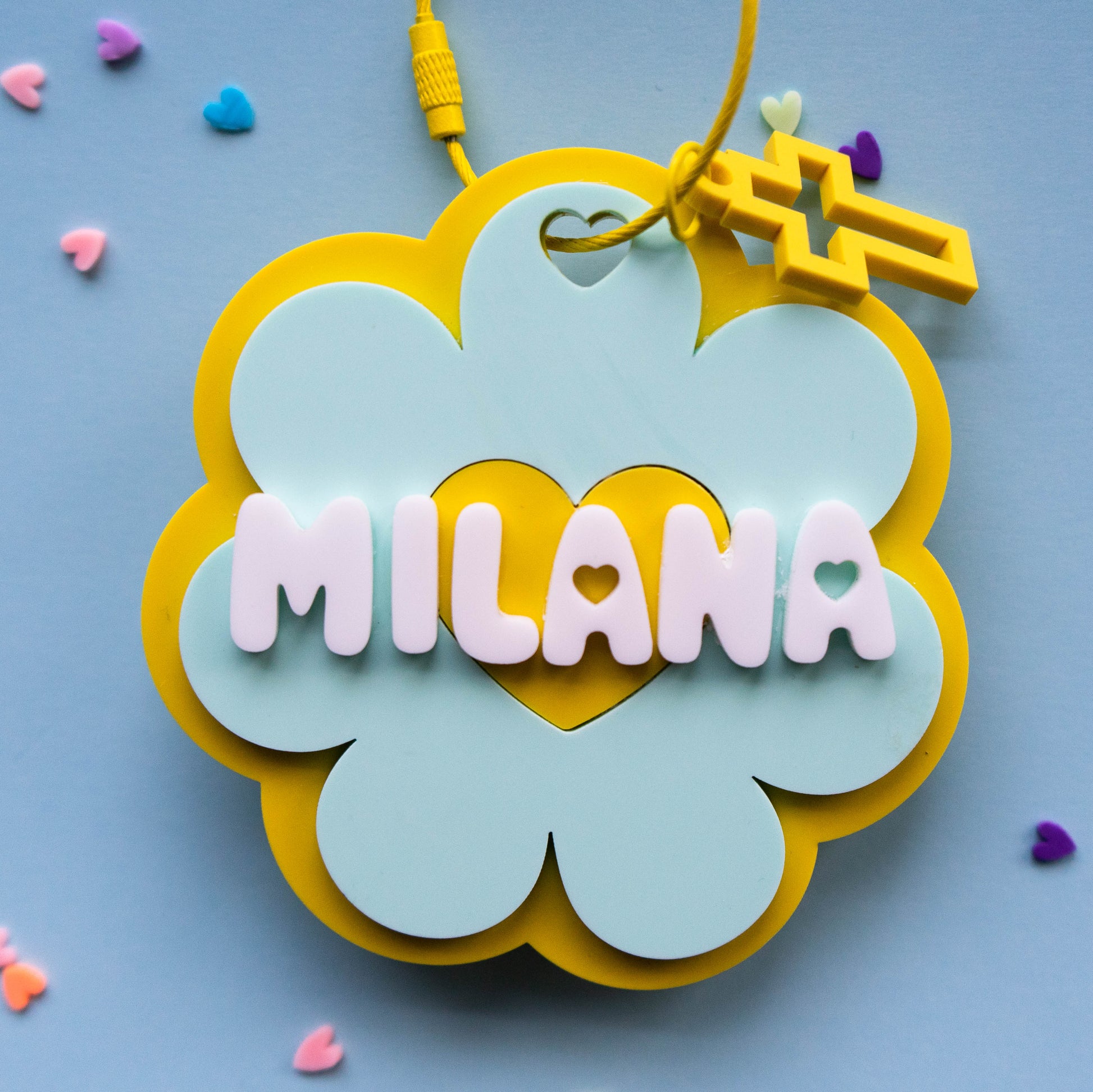 Decorative name tag with 'MILANA' on a blue background with colorful heart-shaped confetti.
