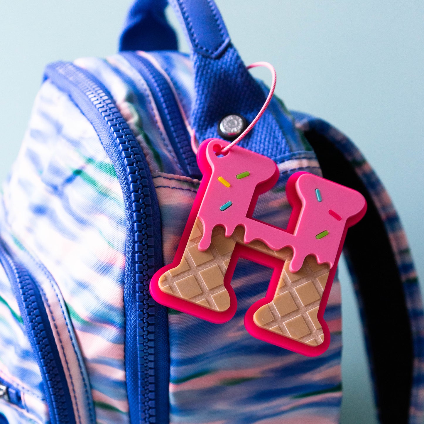 Icecream style acrylic bag tag on a blue pattern backpack.
