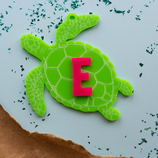 Bright green acrylic turtle bag tag with pink letter “E,” personalized kids backpack charm inspired by ocean animals.